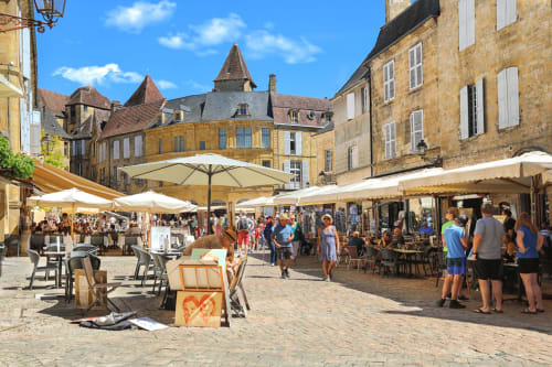 Medieval French village square market in Carsac-Aillac with umbrellas, historic stone buildings, and bustling outdoor vendors