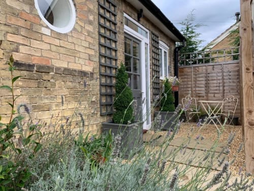 Grapevine Studio courtyard with brick walls, potted plants, lavender, wooden seating, and gravel patio in Waterbeach,