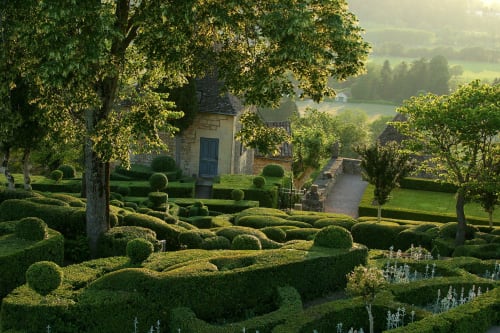 Lush formal gardens with manicured hedges at Domaine De Campagnac B&B in Carsac-Aillac, France, featuring stone buildings and