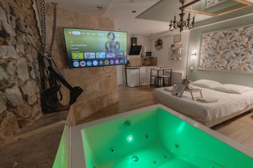 Découvrez la Love Room 3, une suite romantique idéale pour une escapade en couple. Avec ses magnifiques murs en pierre apparents, cette chambre offre une ambiance chaleureuse et authentique. Profitez d'une double vasque moderne et d'un grand écran TV avec Netflix pour vos soirées détente. Le clou du séjour ? Une superbe baignoire à balnéothérapie pour deux, parfaite pour un moment de relaxation absolue. Réservez la Love Room 3 et vivez une expérience inoubliable.