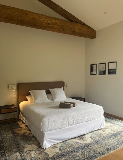 Modern bedroom with wooden beams, queen bed, white bedding, brown leather headboard, and framed artwork at La Conciergerie De