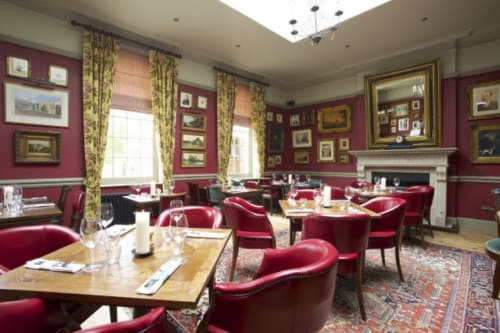 Elegant dining room at Three Little Pigs hotel in Blandford Forum with burgundy walls, gold-framed artwork, red velvet