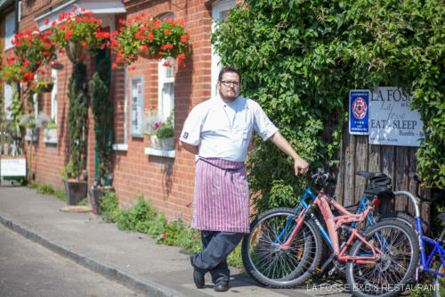Man with bicycle outside La Fosse restaurant in Blandford Forum, red-brick building with hanging flowers and ivy