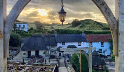 Three Little Pigs hotel in Blandford Forum viewed through wooden archway with hanging lantern, countryside hills beyond