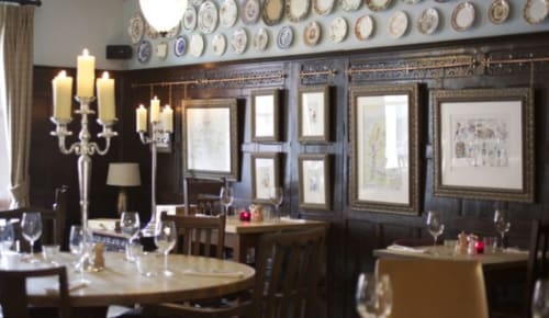 Elegant dining room at Three Little Pigs hotel in Blandford Forum with dark wood paneling, decorative plates, and candlelit
