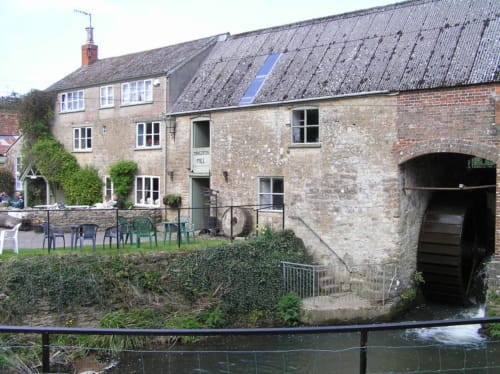 Three Little Pigs hotel in Blandford Forum with stone buildings, outdoor seating, and watermill next to stream