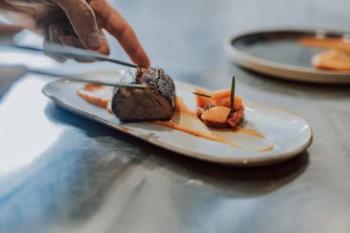 Chef bereid een gastronomisch gerecht op bij Baccara Lodge, Arengosse met geroosterd vlees en groenteversiering