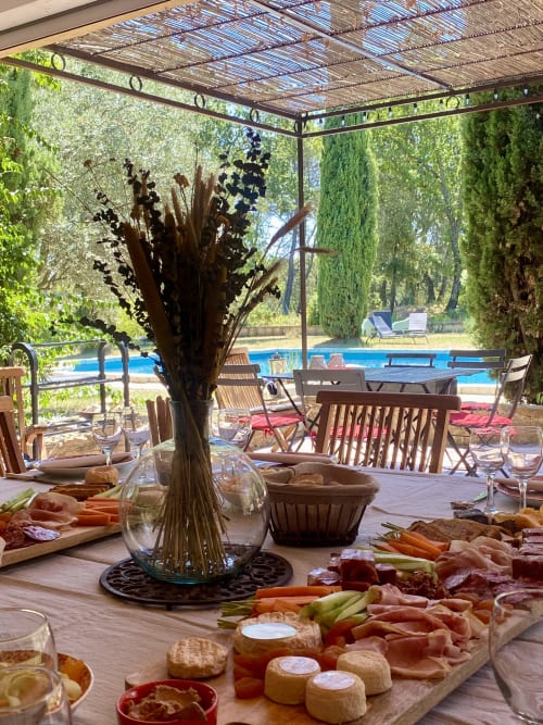 Elegant poolside dining at Domaine Du Commandeur with charcuterie spread, cypress trees and blue pergola in Mondragon