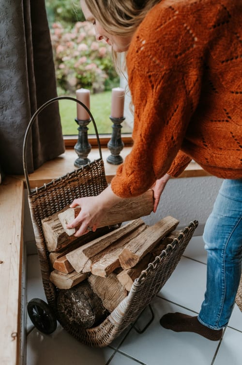 Guest arranging firewood in woven basket at Gîtes du Bulz, Pleyber-Christ, with candles and garden view