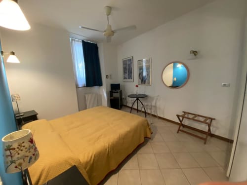 Camera spaziosa presso Alloggio Le Casette a Verona con biancheria gialla, ventilatore a soffitto, specchio rotondo e arredi moderni