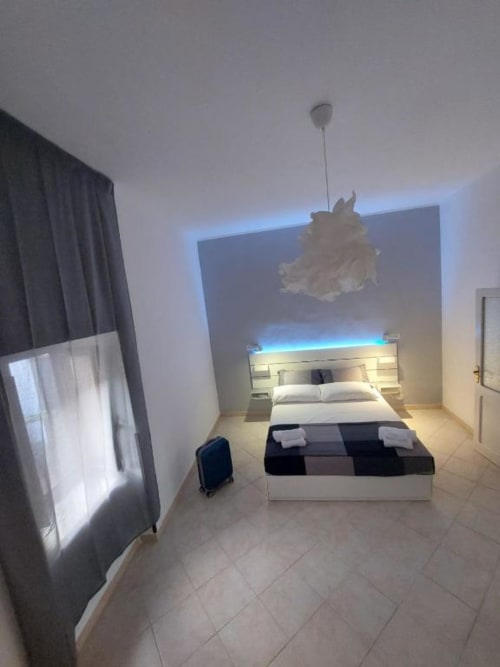 Camera moderna di Sikelia House Cefalù con testata LED blu, biancheria bianca e vista sulla città