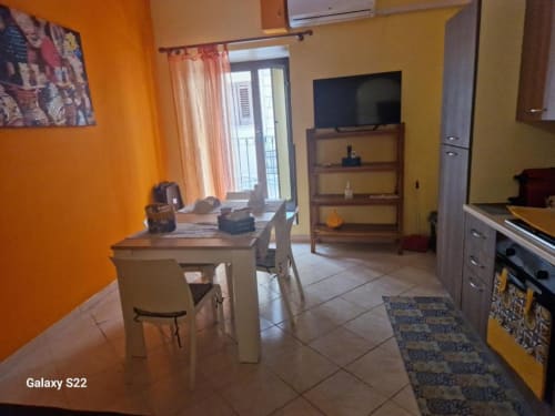 Luminoso appartamento open-plan a Cefalù con pareti arancioni, tavolo da pranzo, cucina, TV, scaffali e vista sulla città dal balcone