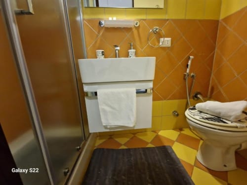 Bagno moderno con lavabo bianco, WC, doccia e piastrelle a motivi geometrici arancioni presso l'appartamento Sikelia House a Cefalù, Sicilia