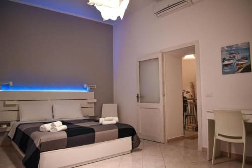 Camera moderna della Sikelia House Cefalù con letto matrimoniale, illuminazione blu, pareti bianche e porte verso il bagno e
