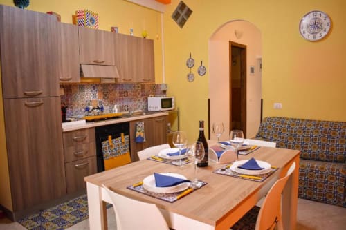 Zona cucina-sala da pranzo in stile siciliano con mobili in legno, piastrelle colorate, tavolo preparato e pareti gialle a Sikelia