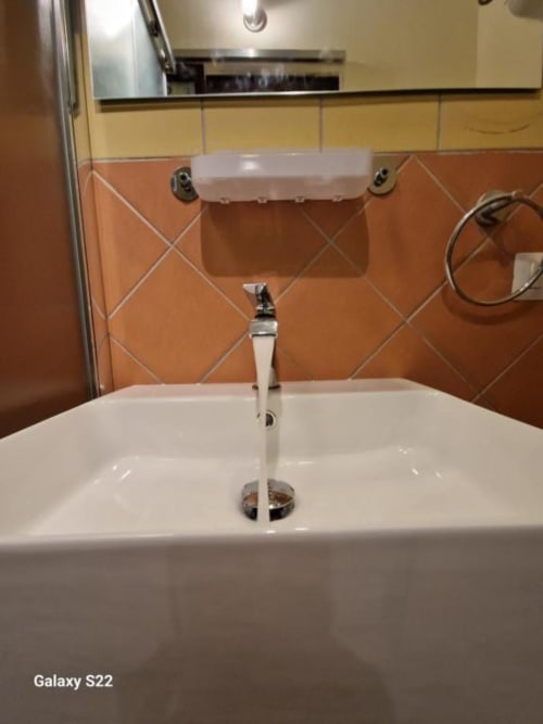 Moderno lavabo da bagno con rubinetto cromato, piastrelle arancioni a motivo geometrico e specchio nell'appartamento Sikelia House a Cefalù, Sicilia