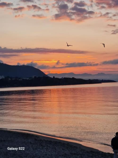 Tramonto sulla costa di Cefalù con montagne, spiaggia e uccelli che volano sopra le acque tranquille di Sikelia House