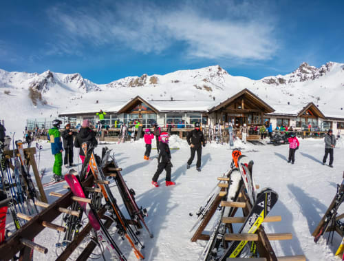 Busy ski resort village with snow-covered mountains, alpine lodge buildings, and skiers with equipment at Vezza d'Oglio