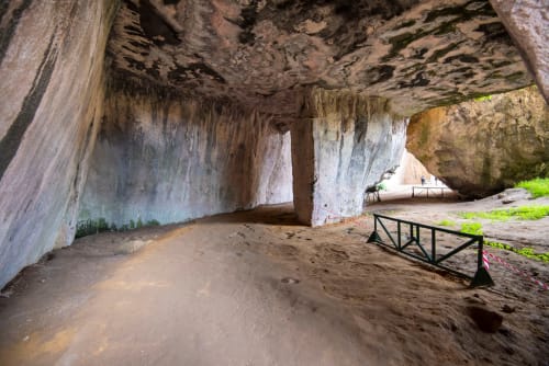 Noemi Holiday House cave entrance with sandy floor, white pillars, and metal railing in Agnone Bagni