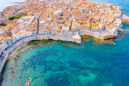 Aerial view of Agnone Bagni coastal town with terracotta buildings, crystal turquoise waters, and sandy beaches