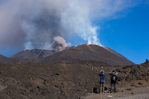 Hikers viewing active volcano with smoke plume near Agnone Bagni, Sicily