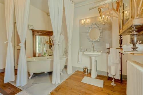 Luxurious bathroom at Baccara Lodge with clawfoot tub, pedestal sink, ornate mirror, and wooden floors