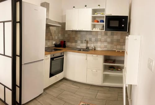 Modern kitchen in Noemi Holiday House apartment with white cabinets, wooden counters, beige tile backsplash, and stainless