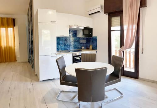 Talìa apartment at Noemi Holiday House with modern white kitchen, blue tile backsplash, round dining table, and sea view