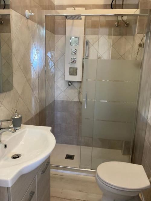 Modern bathroom with walk-in shower, white sink, toilet, and beige tile at Noemi Holiday House, Agnone Bagni