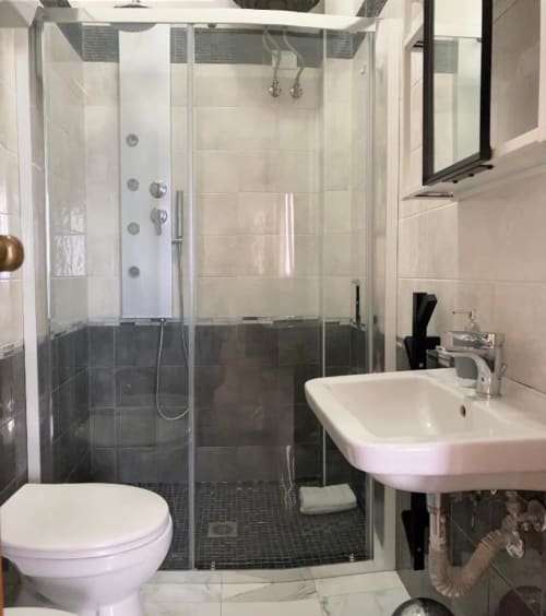 Modern bathroom at Noemi Holiday House with glass shower enclosure, white sink, toilet, and dark tile accents in Agnone Bagni