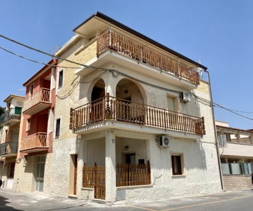 Noemi Holiday House in Agnone Bagni, Italy - three-story cream and terracotta building with wooden balconies and sea views
