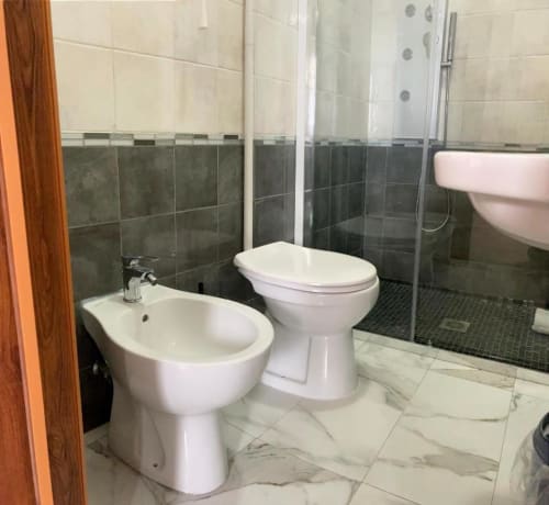 Modern bathroom at Noemi Holiday House with white bidet and toilet, dark tile shower enclosure, marble flooring