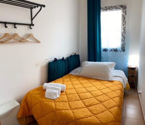 Bright bedroom with yellow quilted bedcover, white pillows, dark teal headboard, and sea view at Noemi Holiday House, Agnone