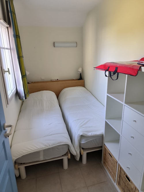 Deux lits jumeaux dans une chambre compacte de l'appartement Loc'Maria à Belle Île en Mer, avec fenêtre et mobilier blanc