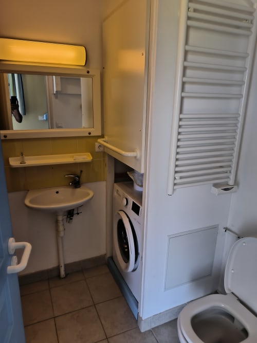 Salle de bain de la Résidence N° 56, appartement Belle Île en Mer avec lavabo, miroir, machine à laver, porte-serviettes et toilettes