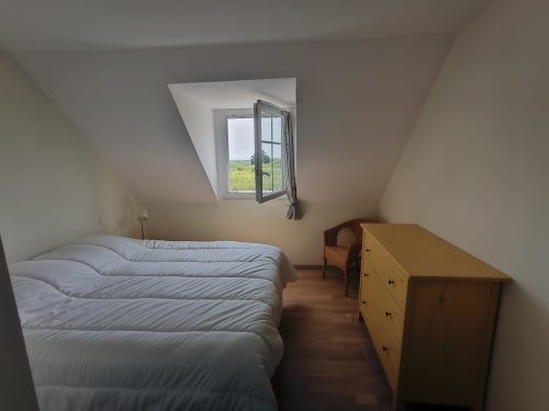 Chambre lumineuse sous les toits à Belle Île en Mer avec vue sur mer par lucarne ouverte, commode en bois et mobilier blanc