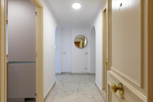 Modern hallway entrance in Marina Banús apartment with marble flooring, cream doors, and circular mirror at Marbella Home