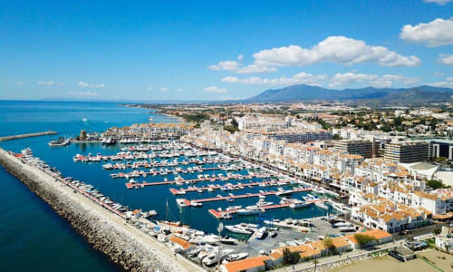 Aerial view of Puerto Banús marina in Marbella with docked boats, Mediterranean Sea, and nearby apartments with city views