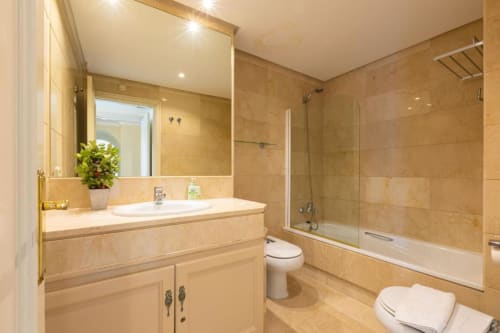 Modern bathroom with marble tiles, vanity sink, toilet, and walk-in shower at Marbella Home Rentals Marina Banús apartment.