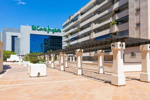Marina Banús apartment complex in Marbella with modern terrace, white columns, and green signage under clear blue sky