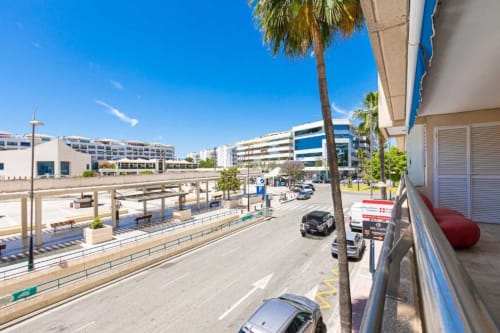 Balcony view of Marina Banús street with palm trees, cars, and modern apartment buildings in Marbella, Spain