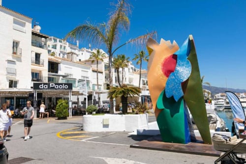 Colorful flower sculpture in Puerto Banús marina with white buildings and palm trees, Marbella
