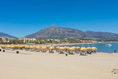 Marbella beach with golden umbrellas, mountain views, and Puerto Banús coastal resort setting