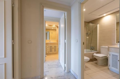 Modern bathroom in Marbella apartment with marble floor, white toilet, vanity, and glass shower enclosure