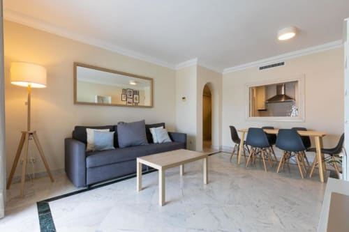 Modern Marina Banús apartment living room with blue sofa, dining table, and kitchen view in Marbella