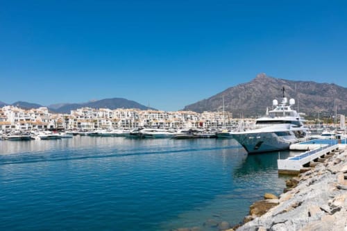Luxury yacht moored at Puerto Banús marina in Marbella with beachfront apartments and mountains in background
