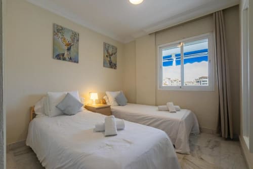 Triple bedroom in Marbella apartment with sea views, white beds, modern decor, and natural lighting