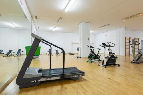 Modern fitness center at Marbella apartment with treadmill, stationary bikes, and gym equipment on wooden floor