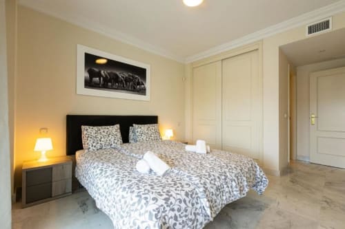 Marbella apartment bedroom with patterned bedding, black headboard, twin lamps, and cream wardrobe doors.