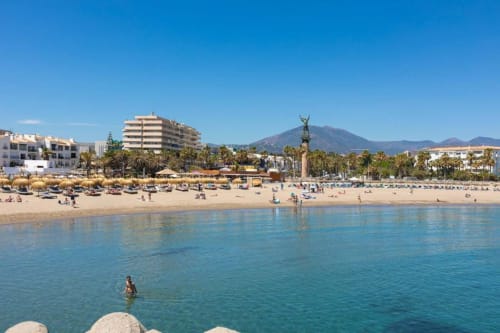 Marbella beach with turquoise water, sandy shore, palm trees, and mountain view in Puerto Banús, Spain